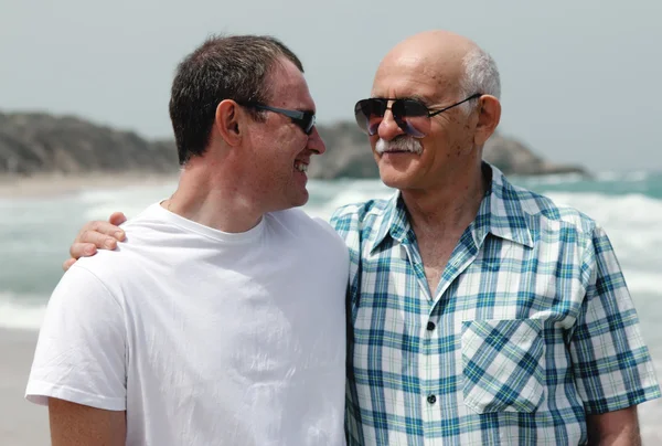 Взрослый сын и отец, гуляющие вместе по пляжу — стоковое фото