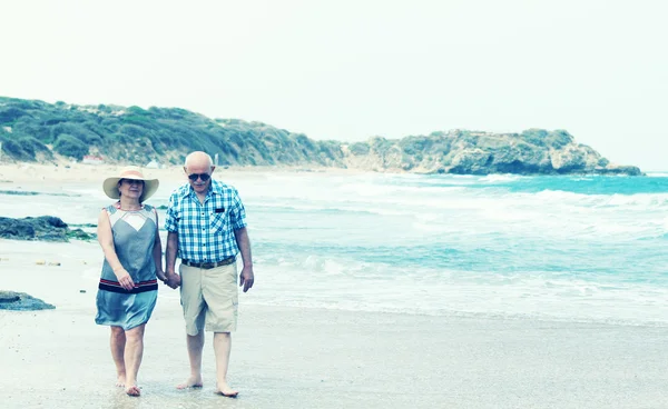 Happy senior couple walking together on a beach. Photo in old image style — Stock Photo, Image