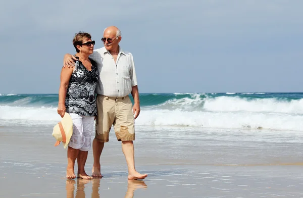 Feliz pareja de ancianos caminando juntos en una playa —  Fotos de Stock