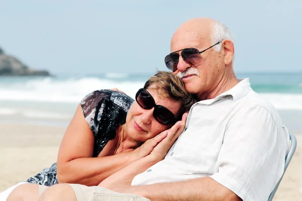 Portrait of happy senior couple sitting together on a beach — Stock Photo, Image