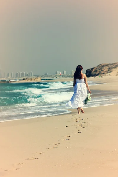 Młoda kobieta w białej sukni spaceru na plaży — Zdjęcie stockowe