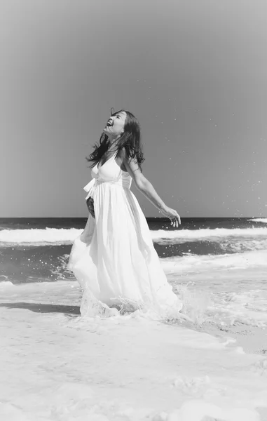 Joven mujer sonriente en vestido blanco de pie en las olas del mar —  Fotos de Stock