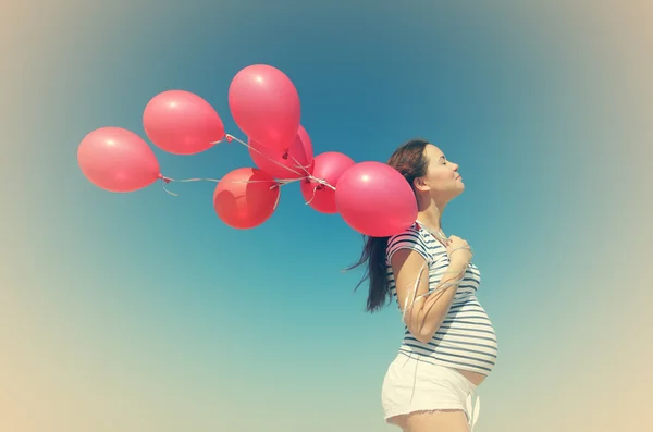 Unga gravid kvinna med röda ballonger — Stockfoto