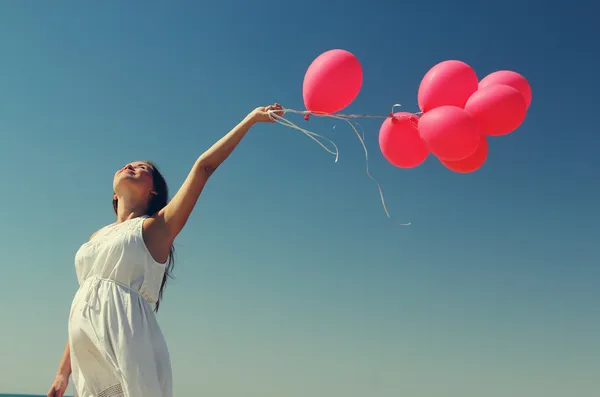 Unga gravid kvinna med röda ballonger — Stockfoto