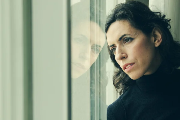 Beautiful 35 year old woman stands in front of the window — Stock Photo, Image