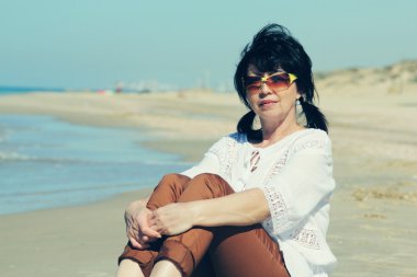 Kadın sahilde oturuyor.
