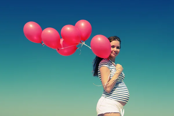 Mujer embarazada joven sosteniendo globos rojos — Foto de Stock