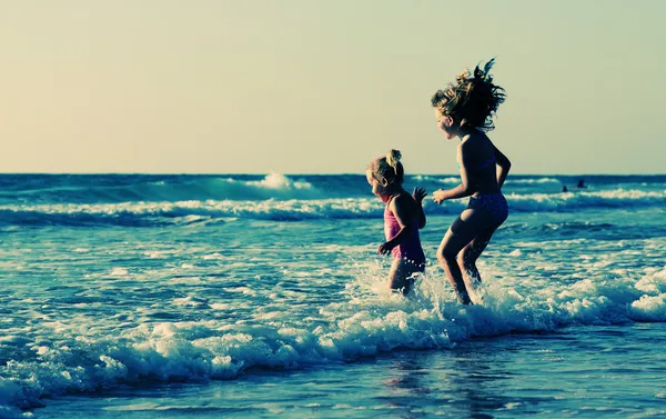 Twee gelukkige jonge geitjes spelen op het strand bij zonsondergang — Stockfoto