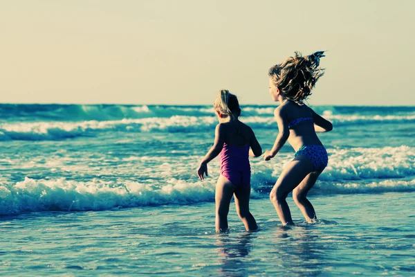 Dvě šťastné děti hrají na pláži při západu slunce — Stock fotografie