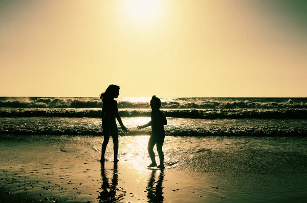 Duas crianças felizes brincando na praia ao pôr do sol — Fotografia de Stock