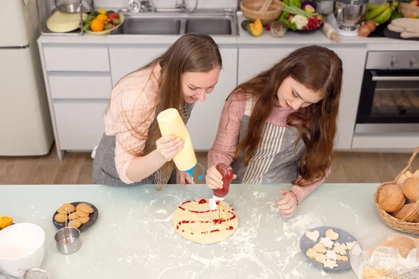 In the kitchen at home, a playful mother and daughter yell while making pizza dough.