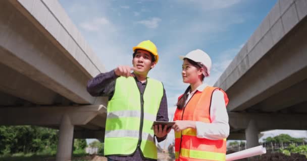 Dwóch Azjatyckich Inżynierów Nosi Kask Kamizelki Bezpieczeństwa Patrząc Planistę Budowy — Wideo stockowe