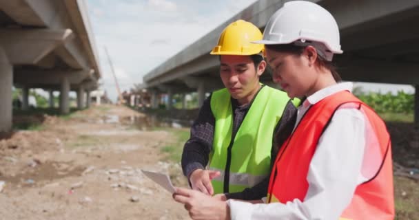Két Biztonsági Mellényt Sisakot Viselő Ázsiai Mérnök Vitatja Meg Projektet — Stock videók