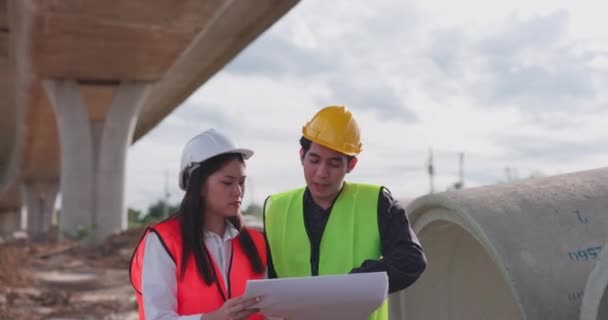 Dos Empleados Ingenieros Asiáticos Que Usan Chalecos Seguridad Cascos Debaten — Vídeo de stock