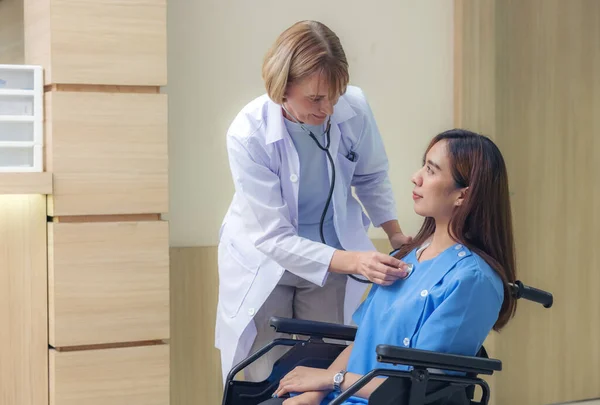 在医院走廊里 一位面带微笑的医生检查了一位病人 一位亚洲妇女瘫痪坐在轮椅上 — 图库照片