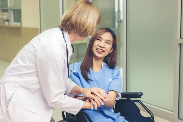 在医院走廊里 一位面带微笑的医生检查了一位病人 一位亚洲妇女瘫痪坐在轮椅上 — 图库照片