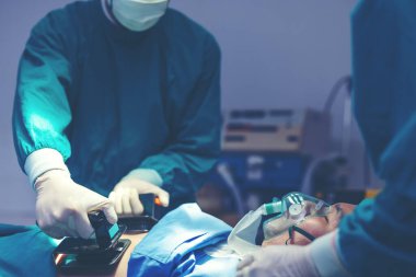 Ameliyathane içinde tıbbi cerrahi yaparken, bir doktor ve hemşire hayatlarını kurtarmak için kalp atışı düşük bir hastanın göğsüne defibrilatör pompalıyor. Acil durumlarda hem kalp masajı hem de ilk yardım mümkün.