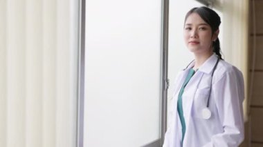 Hastanenin iş yerinde pencerenin önünde poz veren neşeli kızıl saçlı bir kadın doktorun görüntüsü..