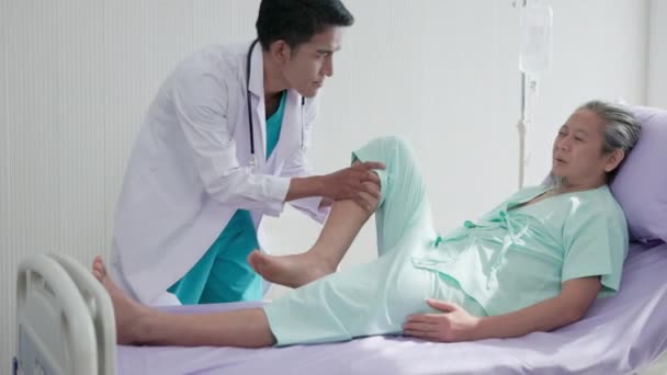 在医院里 一位骨科医生在一位老人躺在病床上检查他的膝盖 医生检查一个老年人的膝盖 — 图库视频影像