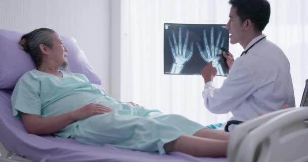 在医院里 一位好心的男性骨科医生和一位躺在病床上的老人讨论了X光扫描 — 图库视频影像