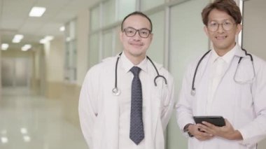 Beyaz önlüklü iki erkek doktor sohbet ediyor, bilgisayar tableti kullanıyor ve el sıkışıyor. Sağlık teknolojisinin yanı sıra sağlık sektöründe ortaklık kavramı.