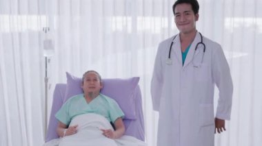 Genç bir Asyalı doktor hastane kayıt bürosunda kendine güvenen yetişkin bir doktorun portresi güvenle gülümsüyor ve çapraz kollarla poz veriyor..