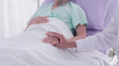 Genç Asyalı bir tıp adamı hasta bir adamın elini tutuyor ve sohbet ediyor. Tıp, yaş, sağlık hizmetleri ve psikiyatristler tıp hakkında düşünürken akla gelen kelimelerdir..