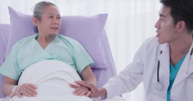 Genç Asyalı bir tıp adamı hasta bir adamın elini tutuyor ve sohbet ediyor. Tıp, yaş, sağlık hizmetleri ve psikiyatristler tıp hakkında düşünürken akla gelen kelimelerdir..