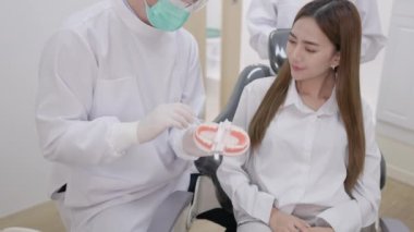Doktor dişçi parmaklarında dişlerin bir kopyasını tutuyor ve erkek bir dişçi sorunu genç bir bayana anlatıyor..