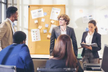 Çok ırklı iş adamları çeşitli ofis çalışanları modern bir ofiste iş arkadaşlarıyla konuşurken ve gülümserken, kıdemli işadamı bir fon sunumu yapıyor
