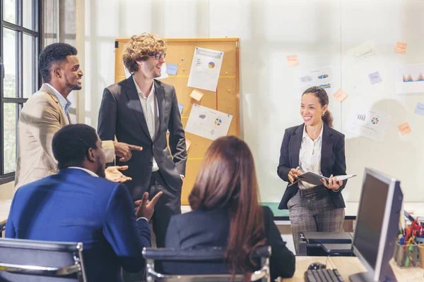 Çok ırklı iş adamları çeşitli ofis çalışanları modern bir ofiste iş arkadaşlarıyla konuşurken ve gülümserken, kıdemli işadamı bir fon sunumu yapıyor