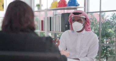 Tıbbi maskeli erkek ve kadın çok ırklı profesyonel işçiler, akşam saatlerinde modern bir kabinede düzenlenen bir takım konferansında iş konuşmasında bulundular.