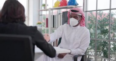 Tıbbi maskeli erkek ve kadın çok ırklı profesyonel işçiler, akşam saatlerinde modern bir kabinede düzenlenen bir takım konferansında iş konuşmasında bulundular.