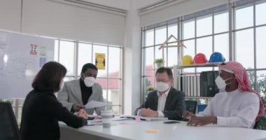 Sosyal uzaklık kavramına ve yeni normal yaşam tarzına sahip biri çok kültürlü iş adamları ve kadınları birlikte çalışırken ve sohbet ederken denetliyor..