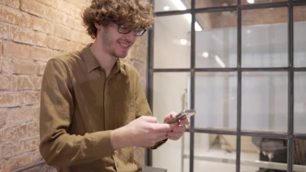 オフィスでは 男性の千年紀の専門家は 現代的なスマートフォンのテキストメッセージを保持しています 職場では 若い男がスマートフォンアプリを使用します — ストック動画