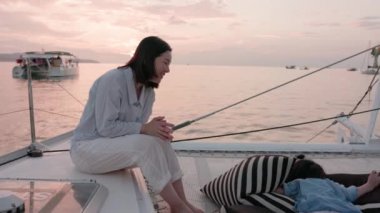 On the boat, an Asian mother and her son. On a yacht resting at sunset, a young boy kisses his mother, who laughs and smiles.