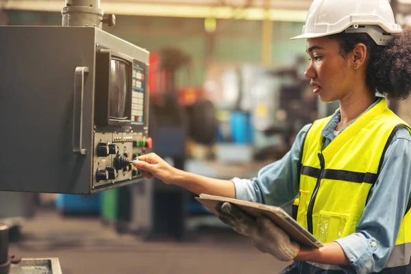 一位头上戴安全帽 手里拿着平板电脑的女工业电气工程师站在控制面板前 检查并维护工厂的数控机床 — 图库照片