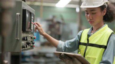 Endüstriyel makineyi kontrol edip kontrol panelinde çalışırken tablet kullanan kendine güvenen zenci kadın fabrika işçisi. Üretim süreci veya makine kavramı