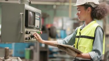 Endüstriyel makineyi kontrol edip kontrol panelinde çalışırken tablet kullanan kendine güvenen zenci kadın fabrika işçisi. Üretim süreci veya makine kavramı