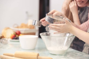 Anne ve küçük çocukları modern bir mutfak alanında neşeli bir şekilde öğrenme, pişirme, pasta süsleme, mutlu küçük kız hafta sonları tatlı hamur işleri hazırlıyorlar.