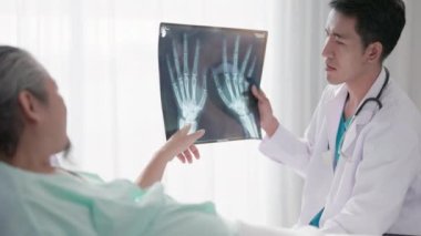 Hastane yatağında bir hastayla konuşan Asyalı bir doktor, bilek kemiğinin röntgenini çeker..