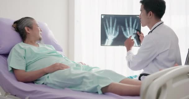 一位亚洲医生在医院病床上与一位病人交谈时 拿着一张他腕骨的X光片 — 图库视频影像