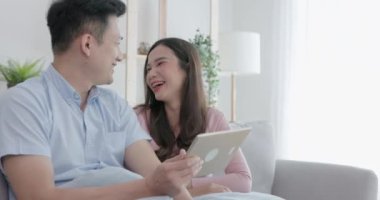 Birkaç Asya kökenli mutsuz adam, elinde dijital tabletle kanepede oturan ortağına bakıyor. 4K çözünürlüğü