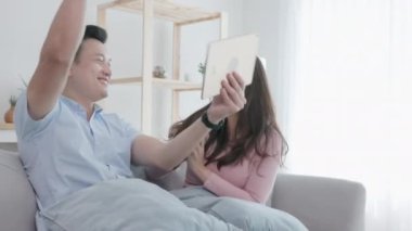 Birkaç Asya kökenli mutsuz adam, elinde dijital tabletle kanepede oturan ortağına bakıyor. 4K çözünürlüğü