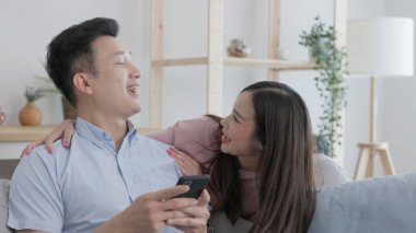 Evdeki kanepede yatarken, mutlu genç bir çift telefonlarını kullanır ve birbirleriyle sohbet ederler..