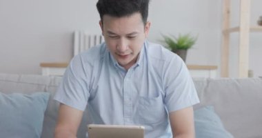 Evde, yorgun orta yaşlı bir adam kanepede yatarken ellerini yüzüne koyar..