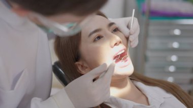 Bir dişçi kliniğinde, üniformalı bir dişçinin aynalı kadın bir hastanın dişlerini tedavi edişinin yan görüntüsü. Bir dişçi diş aynası tutarken muhteşem bir kadının dişleri üzerinde çalışır. Bir konsept olarak dişçilik