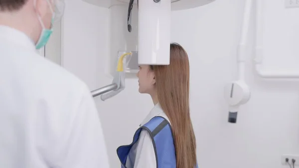 在全景X光机上 牙医把一个女人的咬痕对齐 在一家牙科诊所里 一名身穿铅围裙的妇女站在那里 就像一台全景X光机环绕着她的头 — 图库照片