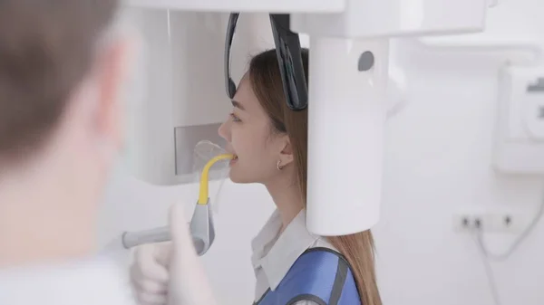 在全景X光机上 牙医把一个女人的咬痕对齐 在一家牙科诊所里 一名身穿铅围裙的妇女站在那里 就像一台全景X光机环绕着她的头 — 图库照片