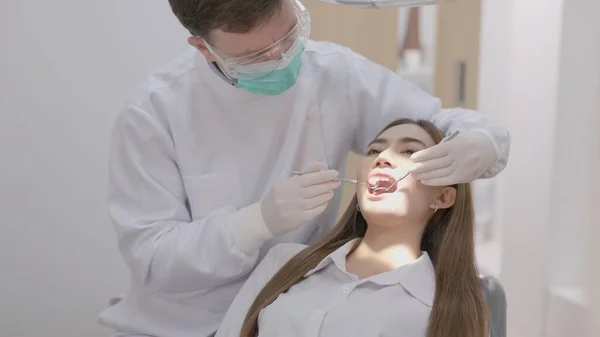 在牙科诊所里 穿着制服的牙医用镜子治疗女病人牙齿的侧视图 牙医拿着牙镜在漂亮女人的牙齿上工作 牙科作为一个概念 — 图库照片